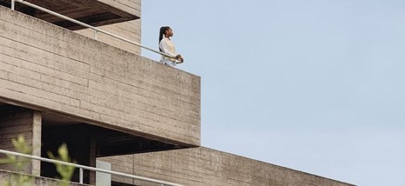 The picture shows a woman standing on a balcony of a concrete building.
